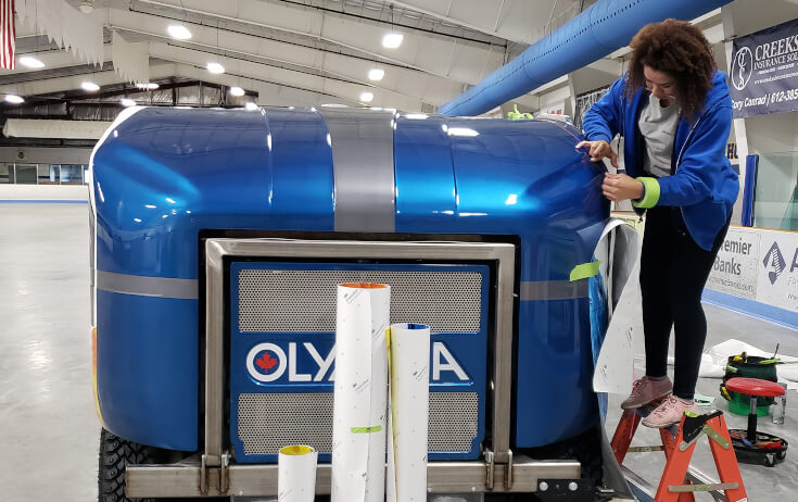 Graphic Production Technician Applying a Vinyl Wrap on a Zamboni